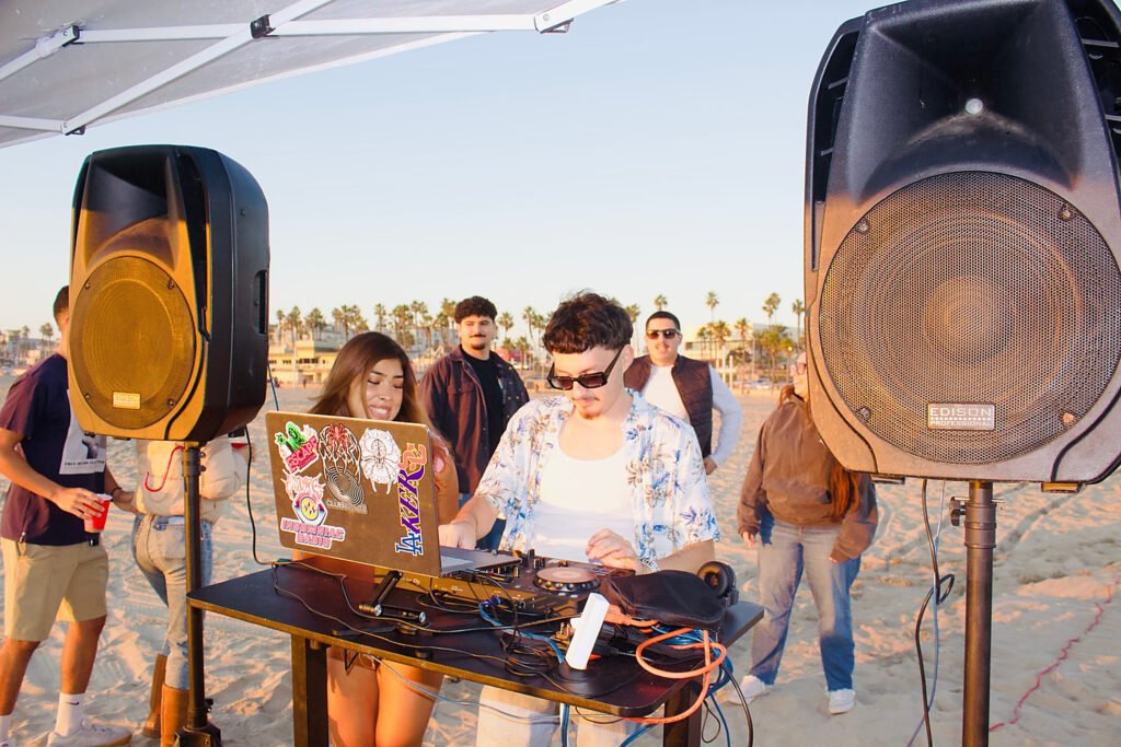 Niko DJing on Venice Beach at sunset with a crowd and speakers